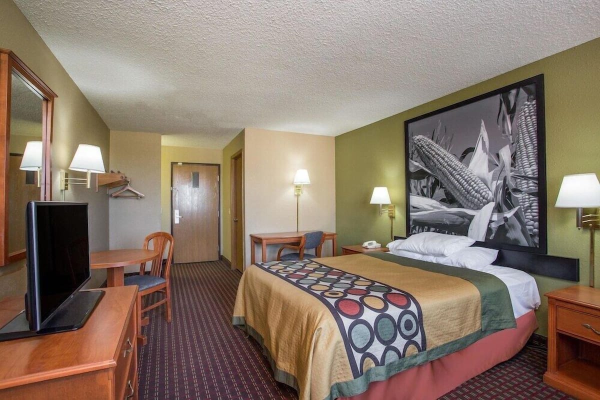 Une chambre d’hôtel équipée d’un lit, d’un bureau, d’une chaise, d’une télévision et ornée d’une grande œuvre d’art au mur.