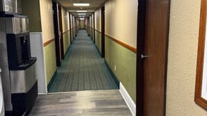 Un couloir d’hôtel avec un long passage, des portes en bois et un coin cuisine équipé d’une machine à café.