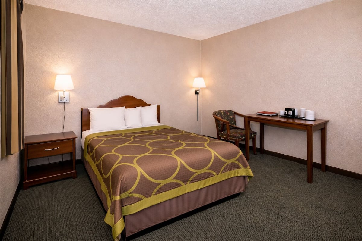 A hotel room with a bed, bedside table, chair, desk, and lamps.