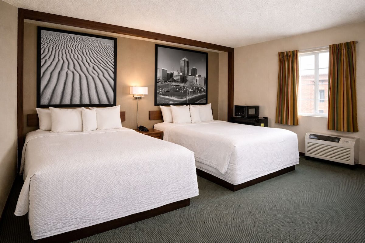 A hotel room with two beds, a flat-screen TV, a heater, and artwork on the walls.