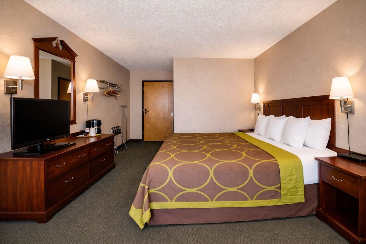 A hotel room with a large bed, a TV, a desk, and a mirror.