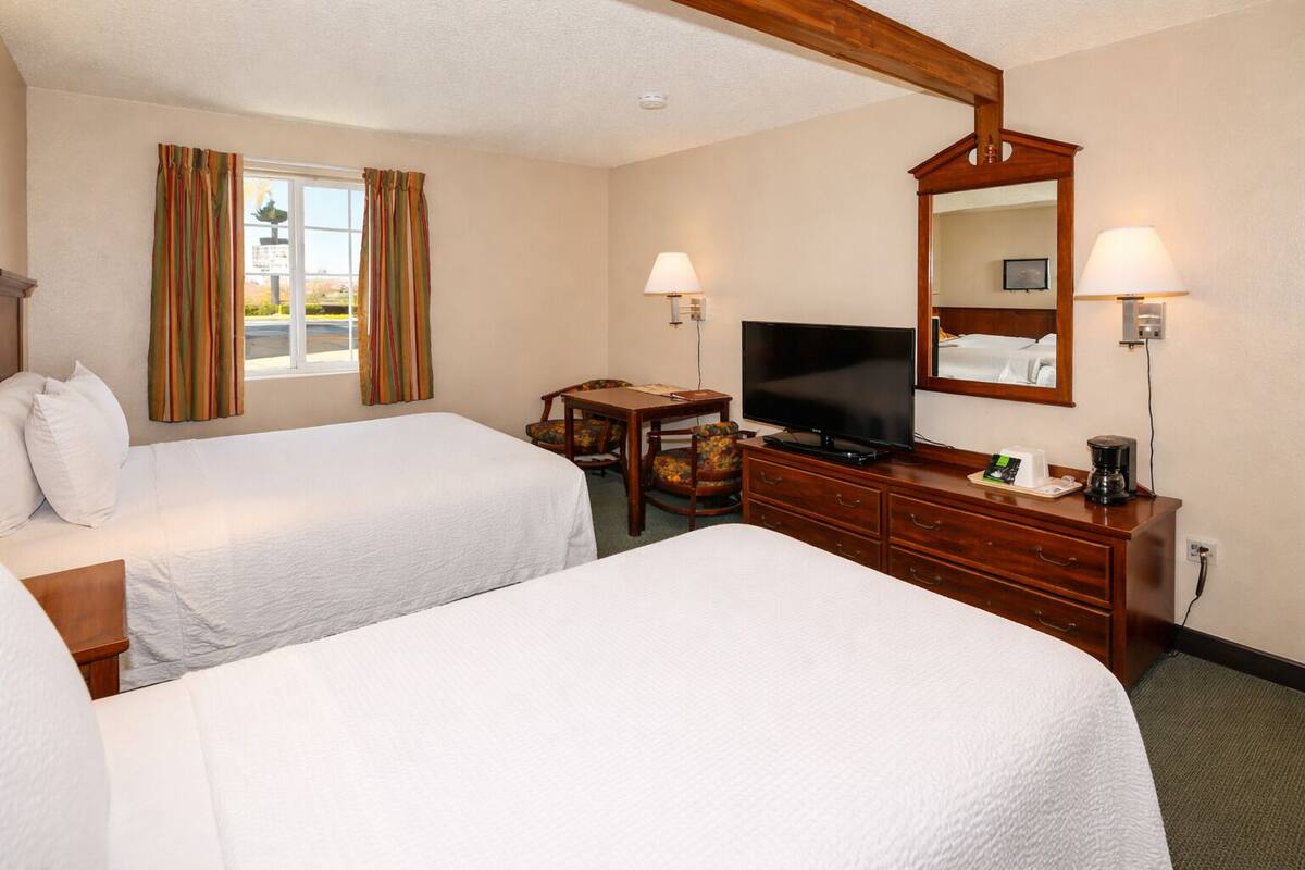 A hotel room with two beds, a desk with a chair, a television, a coffee maker, and a mirror.