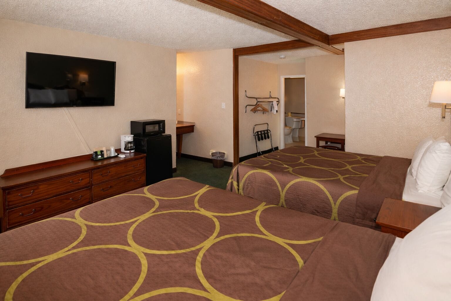 A hotel room with two beds, a dresser, a television, and a small kitchenette.