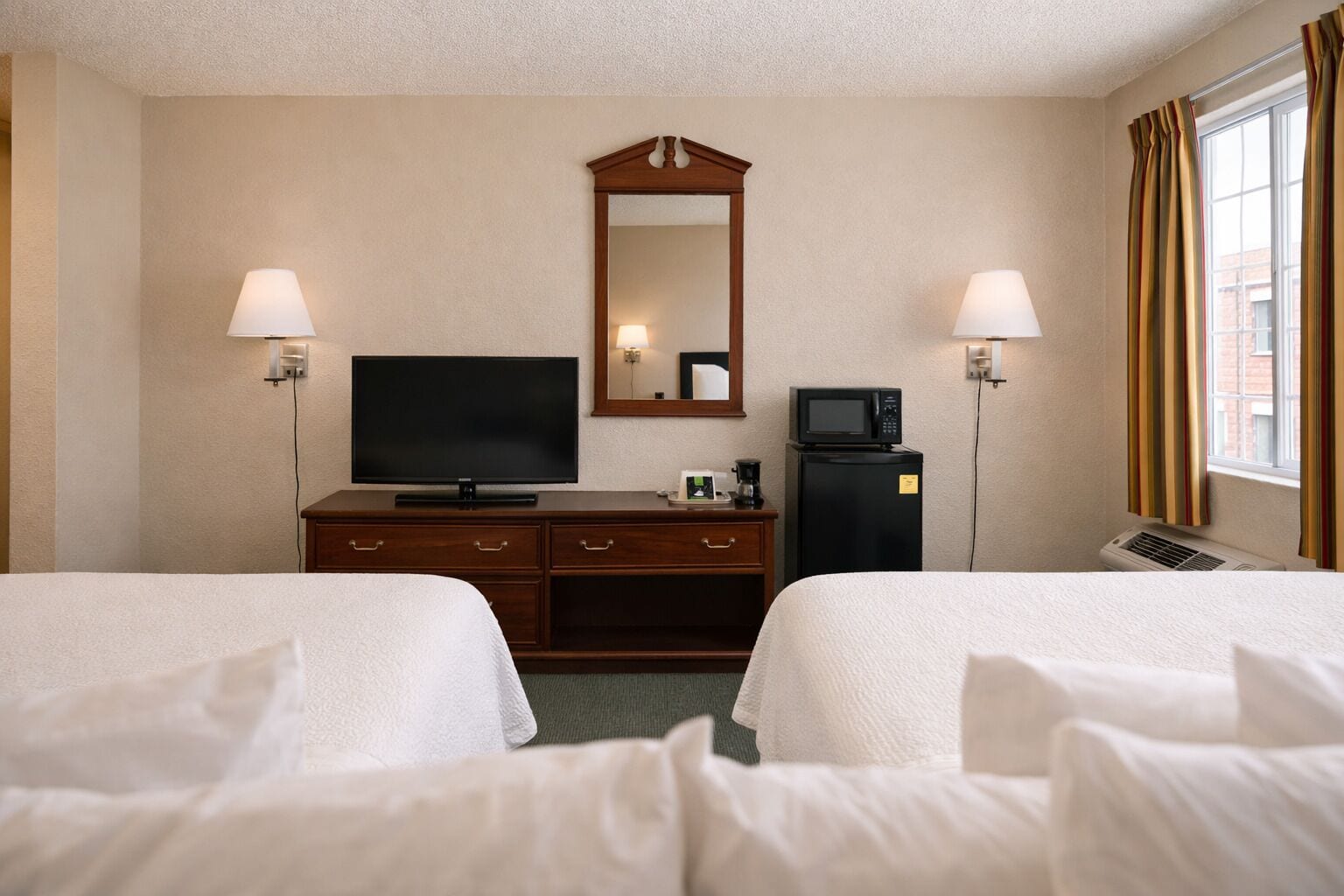 Une chambre d’hôtel avec deux lits, une télévision, un minibar et un miroir.