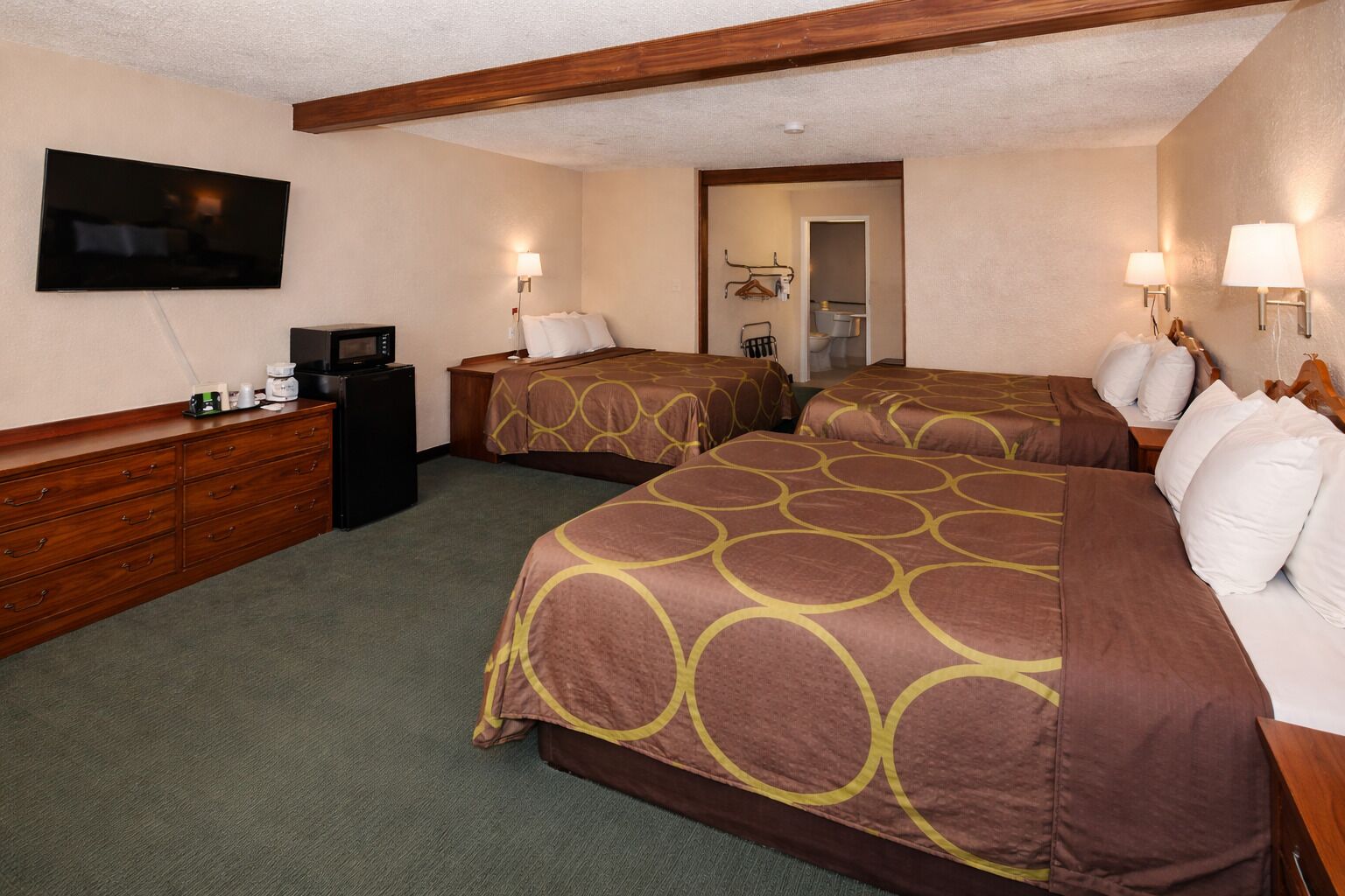 Quarto de hotel com duas camas, televisão, cômoda e banheiro visível por uma porta aberta.