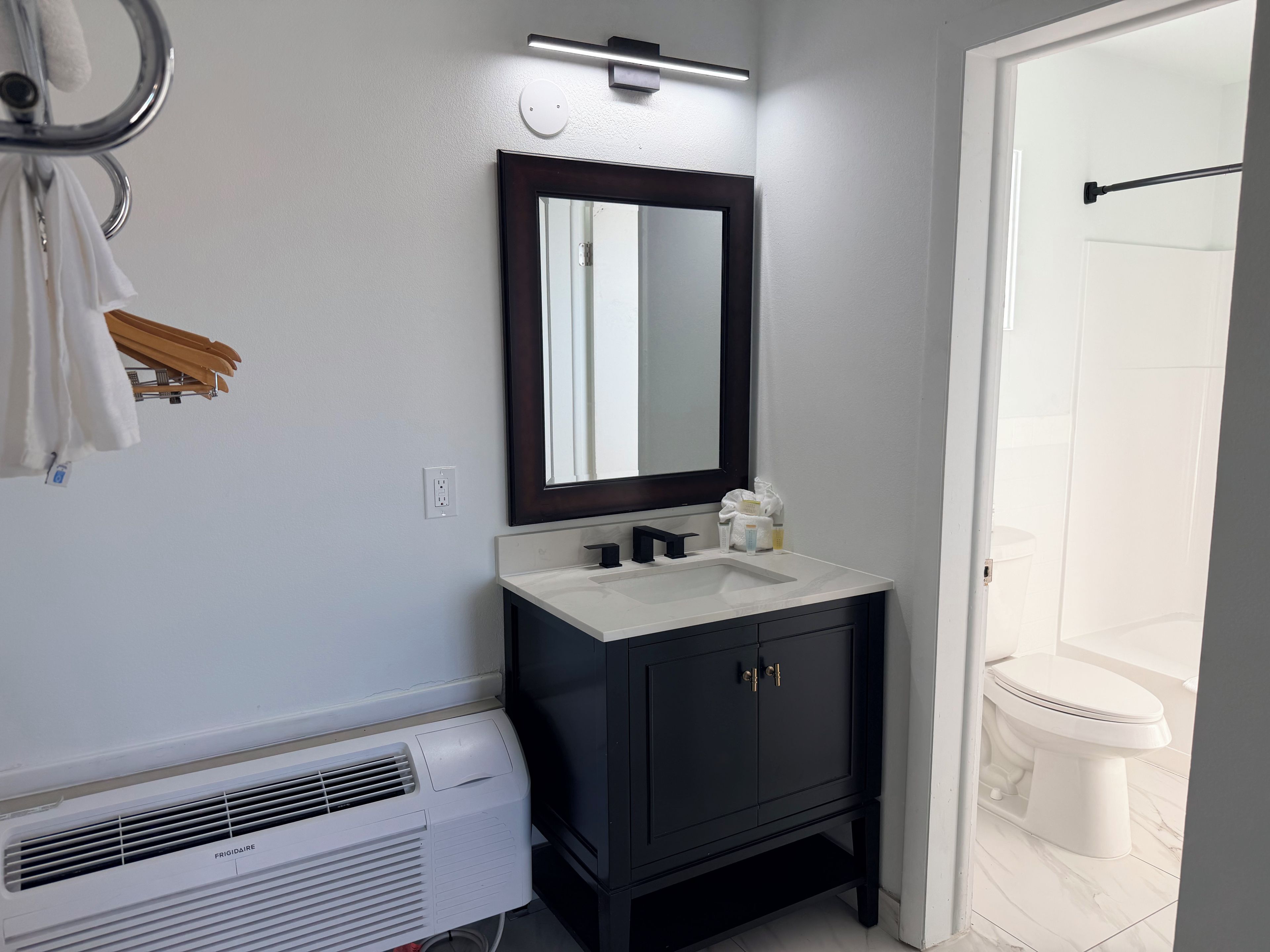 A bathroom with a white sink, dark cabinets, a mirror, and a white toilet.