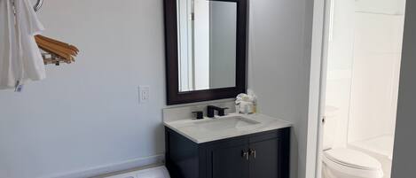 A bathroom with a white sink, dark cabinets, a mirror, and a white toilet.