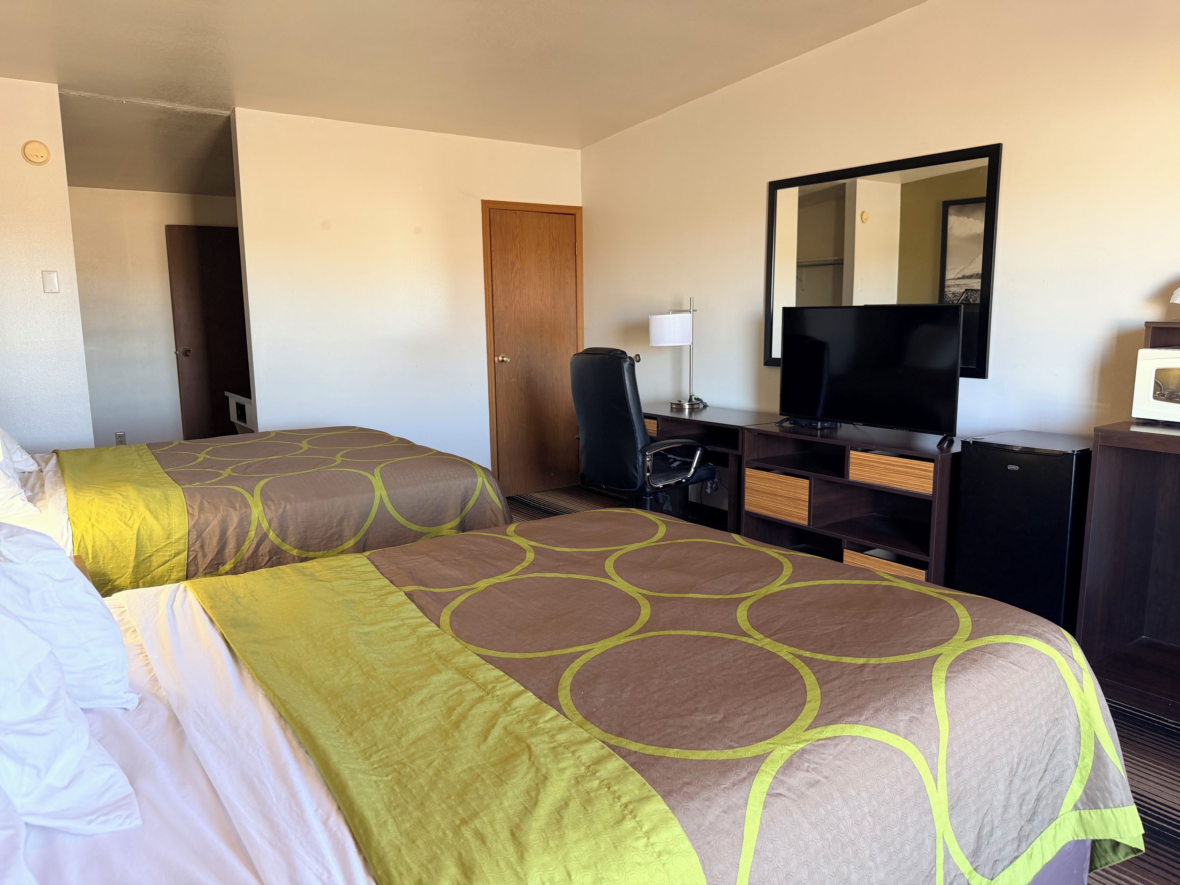 Una habitación de hotel con dos camas, un escritorio con televisor, una silla y un microondas.