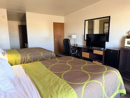 A hotel room with two beds, a desk with a television, a chair, and a microwave.