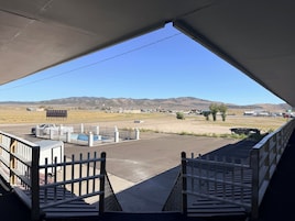 Uma área de estacionamento com piscina cercada, um edifício ao fundo e paisagem montanhosa.