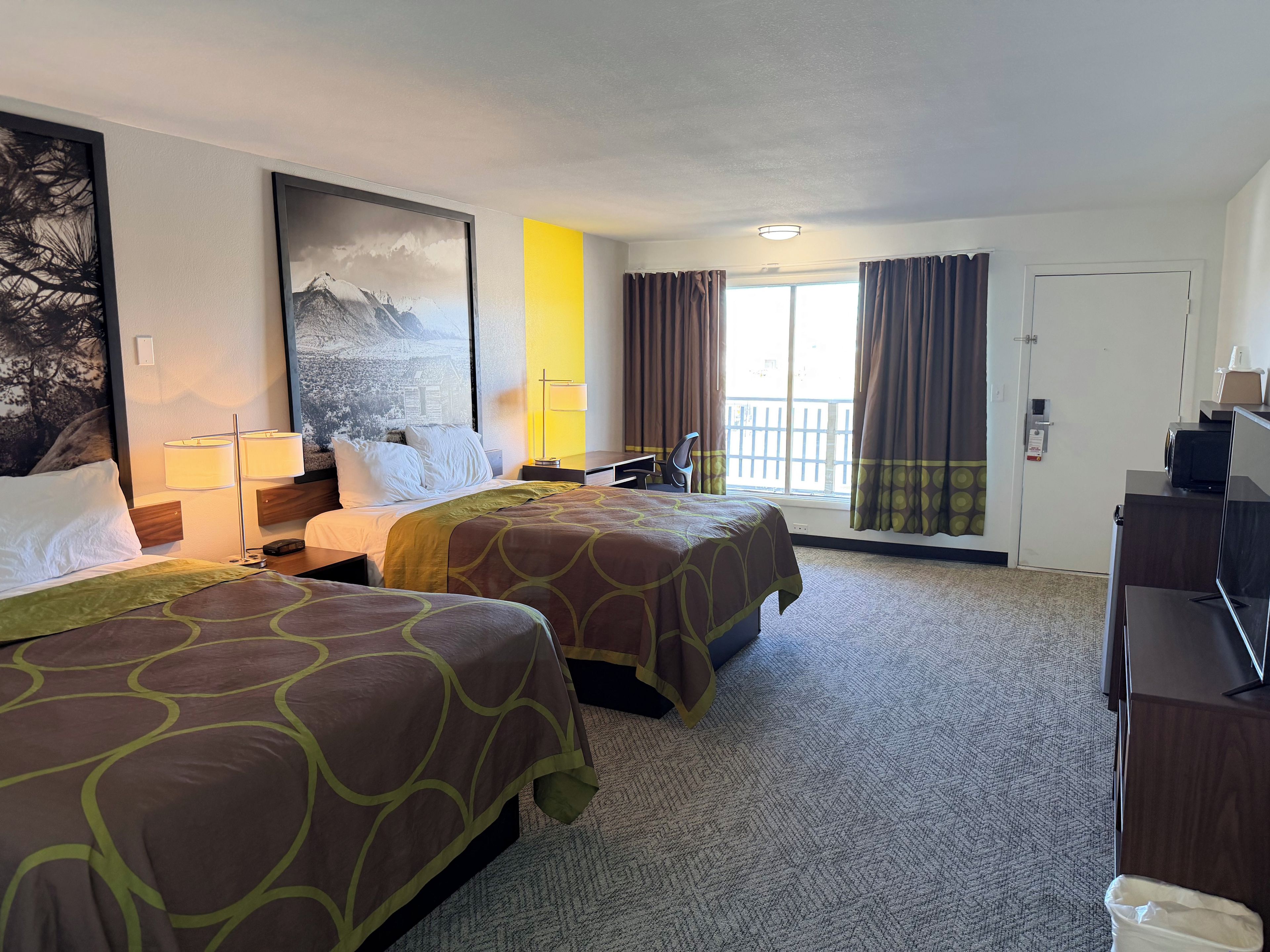 A hotel room with two beds, a desk, a chair, a TV, and a window with curtains.