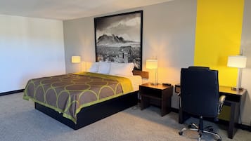 A hotel room with a bed, two bedside tables, a desk with a chair, a large framed picture on the wall, and a carpeted floor.