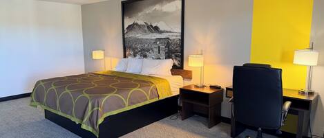 A hotel room with a bed, two bedside tables, a desk with a chair, a large framed picture on the wall, and a carpeted floor.