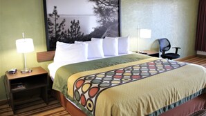 A hotel room with a large bed, a nightstand with a lamp, a chair, and a large window with a view of trees and a body of water.