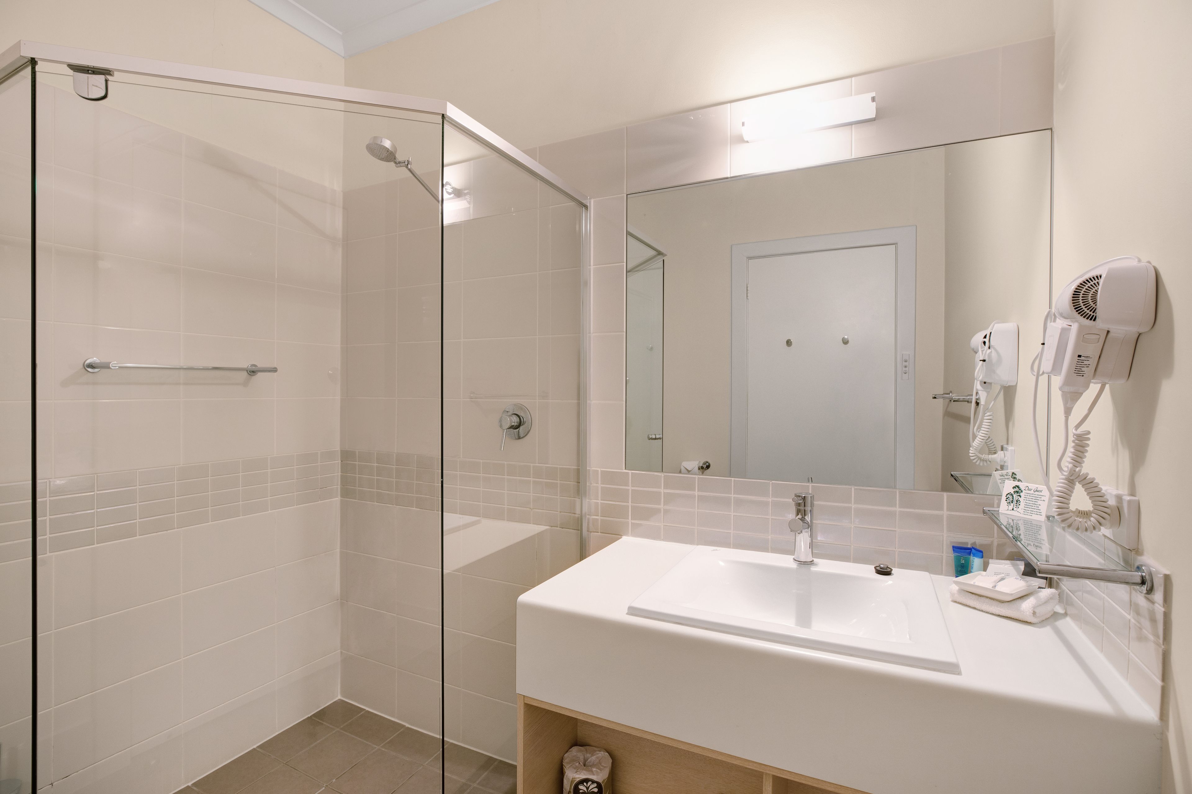 A modern bathroom with a glass shower enclosure, a white sink, and a hairdryer mounted on the wall.