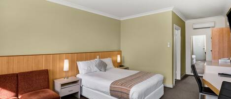 A hotel room with a bed, a desk, a chair, a nightstand, and a sofa.
