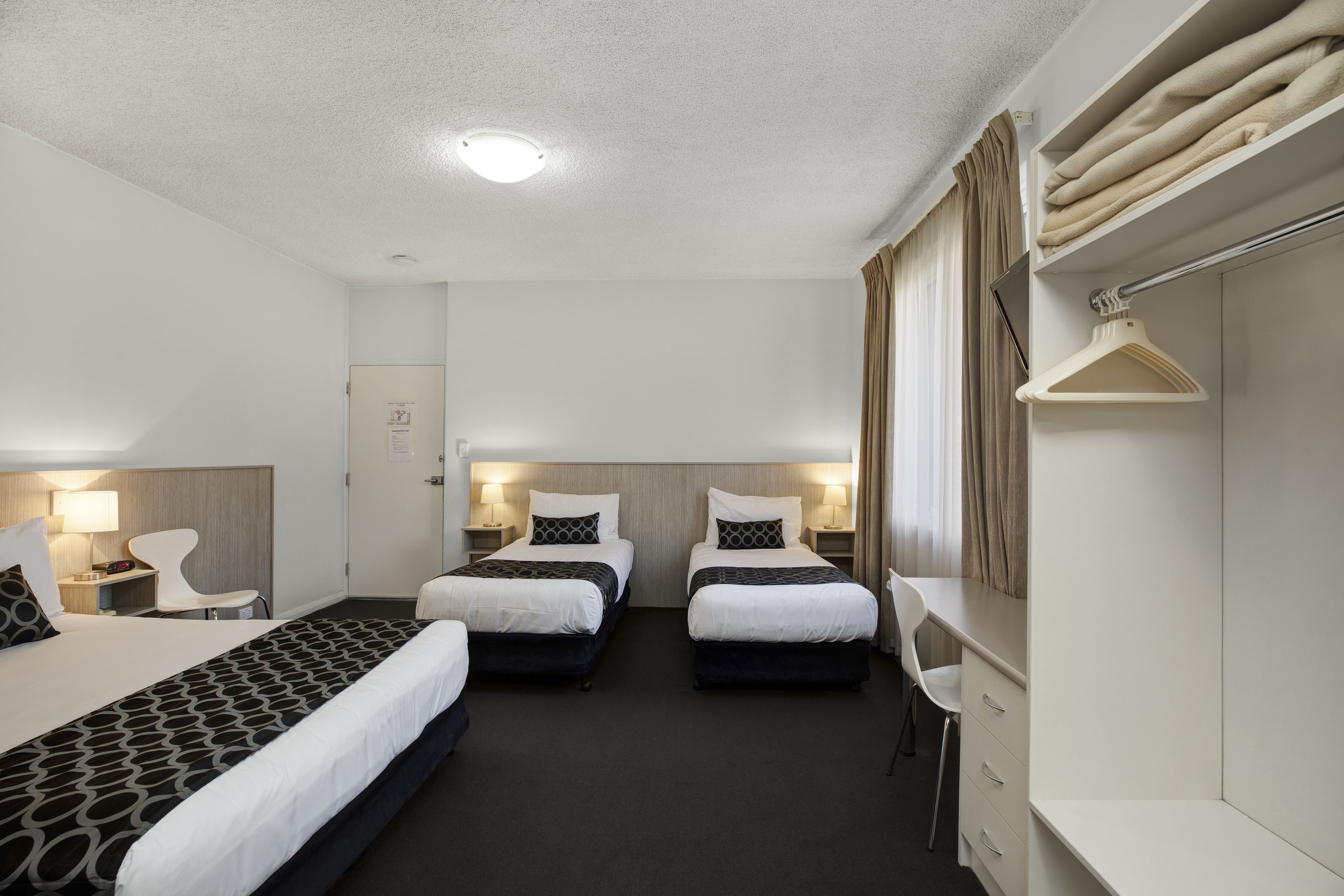 A hotel room with two beds, a desk, a chair, a wardrobe, and a hanging coat rack.