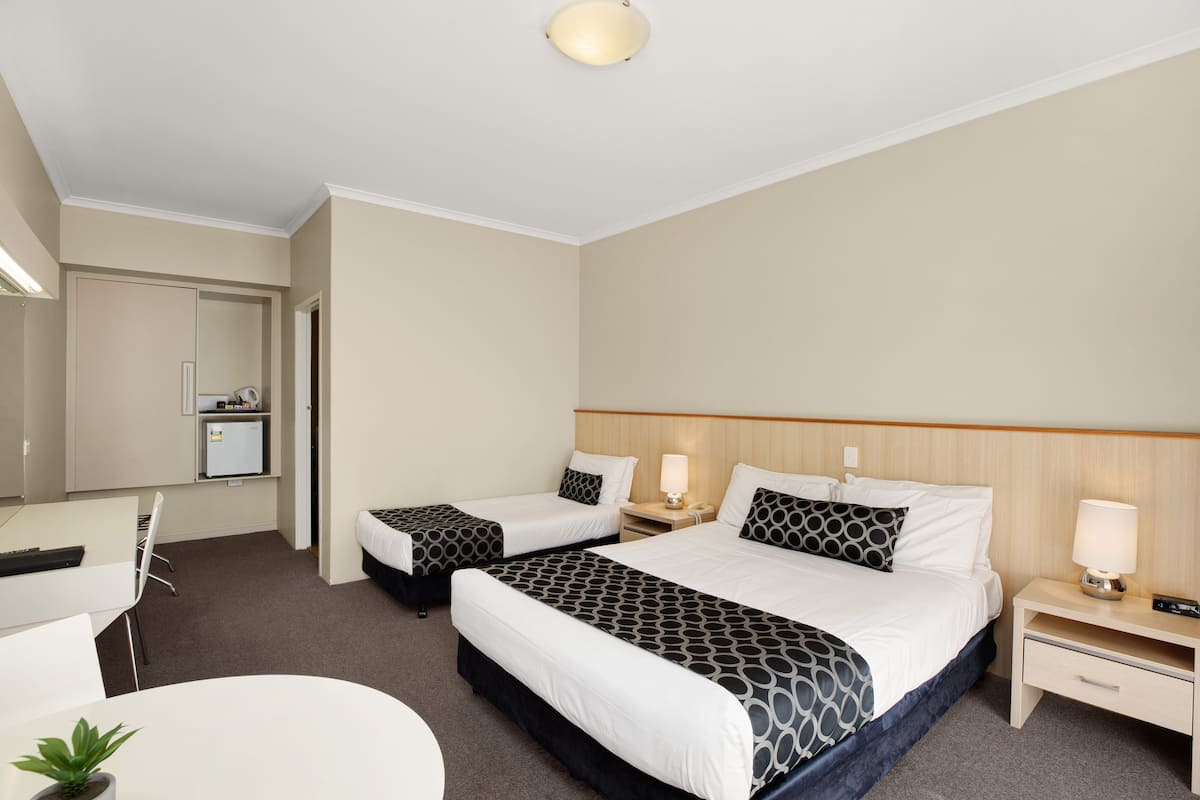 Ett hotellrum med två sängar, ett skrivbord, en stol, ett litet bord, en lampa och ett kylskåp.