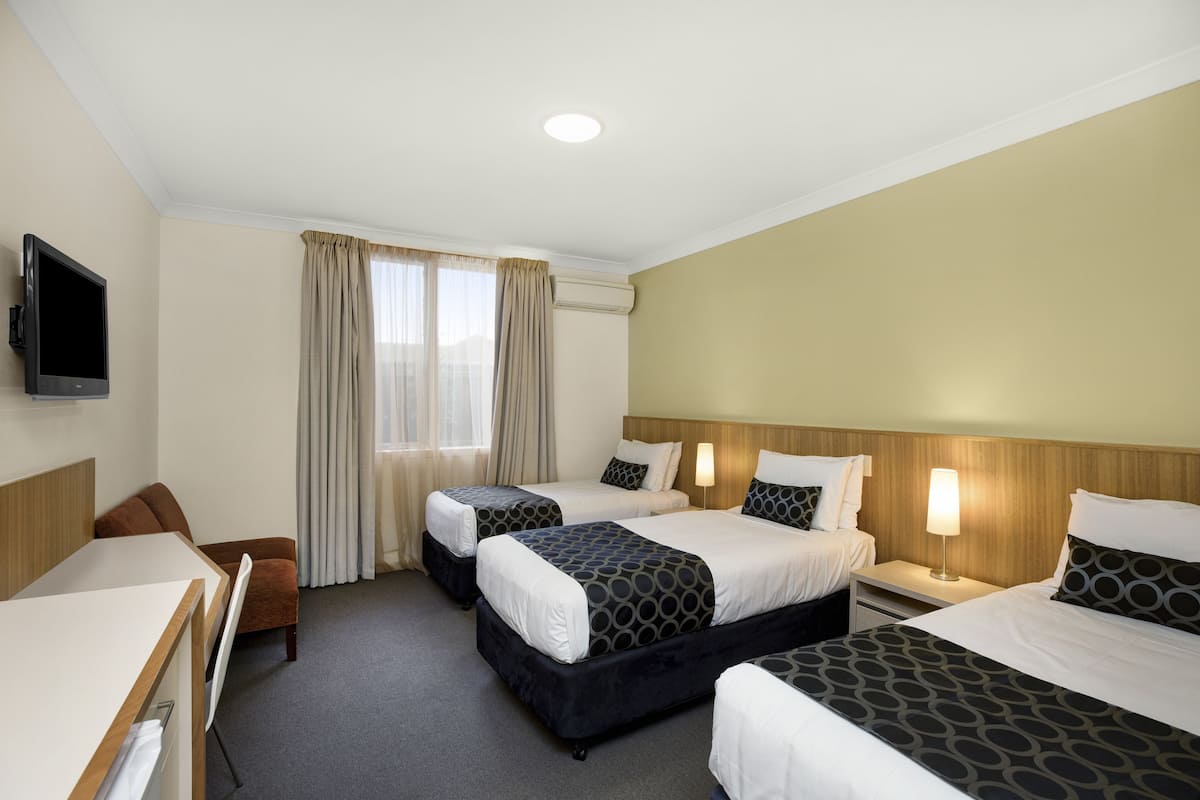 Ett hotellrum med två sängar, ett skrivbord, en stol, en TV och ett fönster med gardiner.