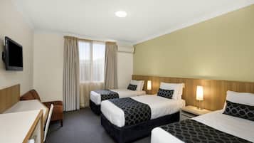 A hotel room with two beds, a desk, a chair, a TV, and a window with curtains.