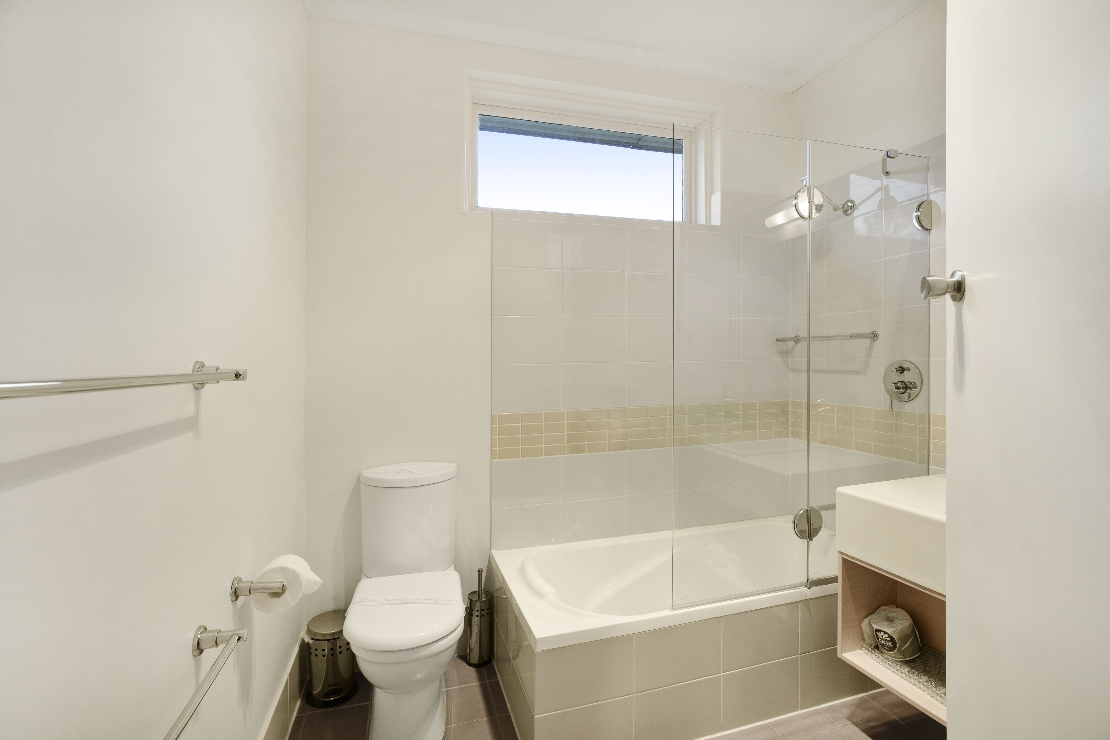 Une salle de bain avec une douche à parois de verre, des toilettes blanches, une baignoire et une petite fenêtre.