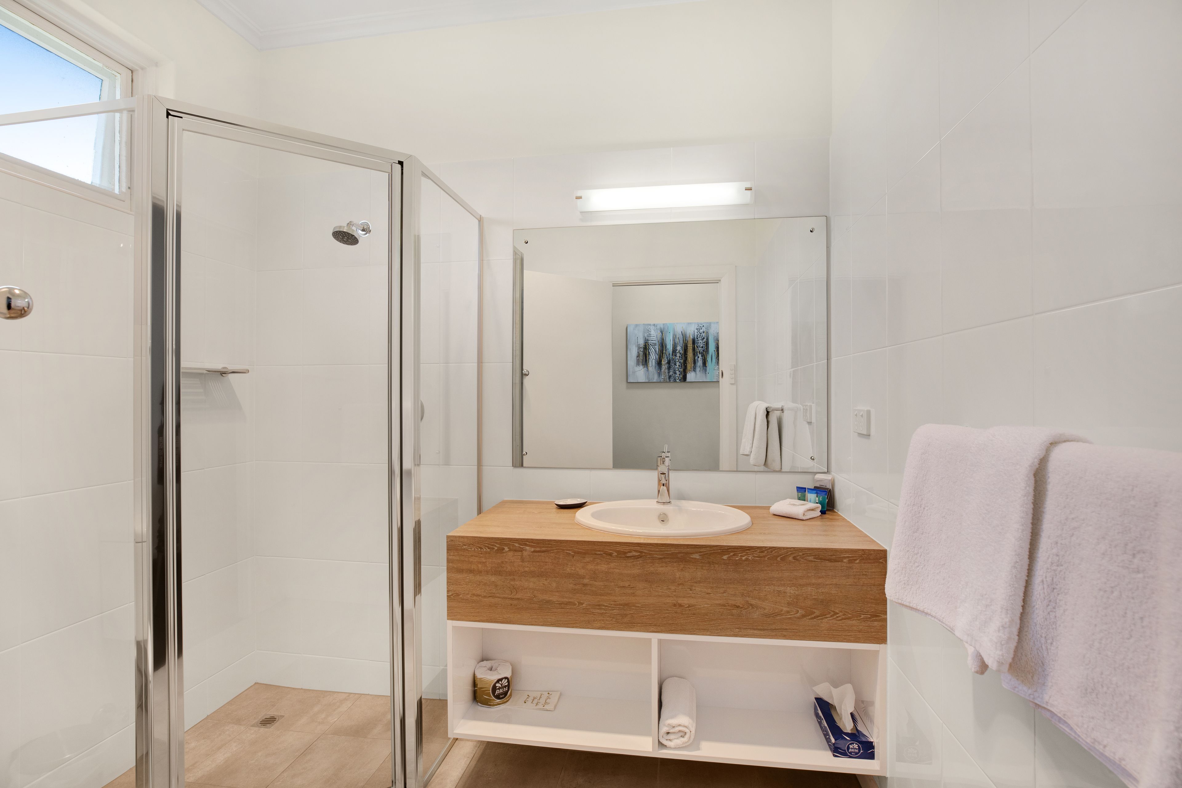 Un baño moderno con cabina de ducha de vidrio, tocador de madera, lavamanos blanco y un espejo grande.