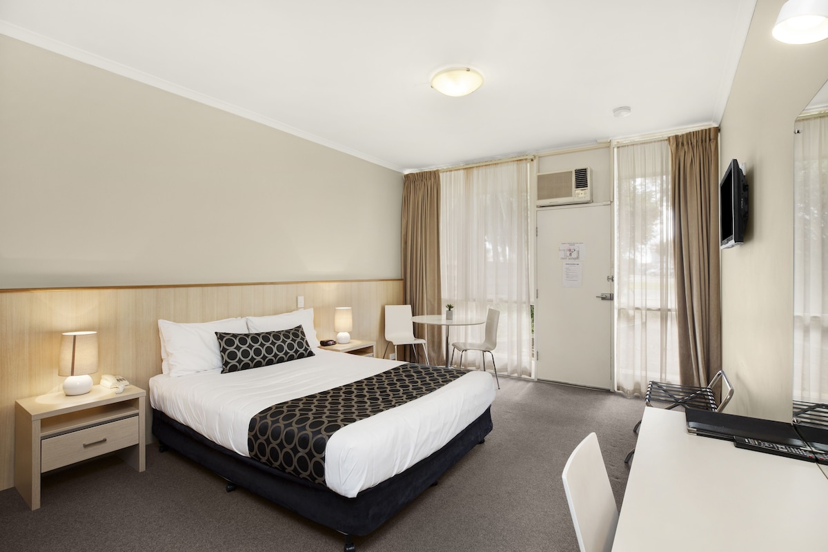 A hotel room with a bed, bedside tables, a desk, and a TV.