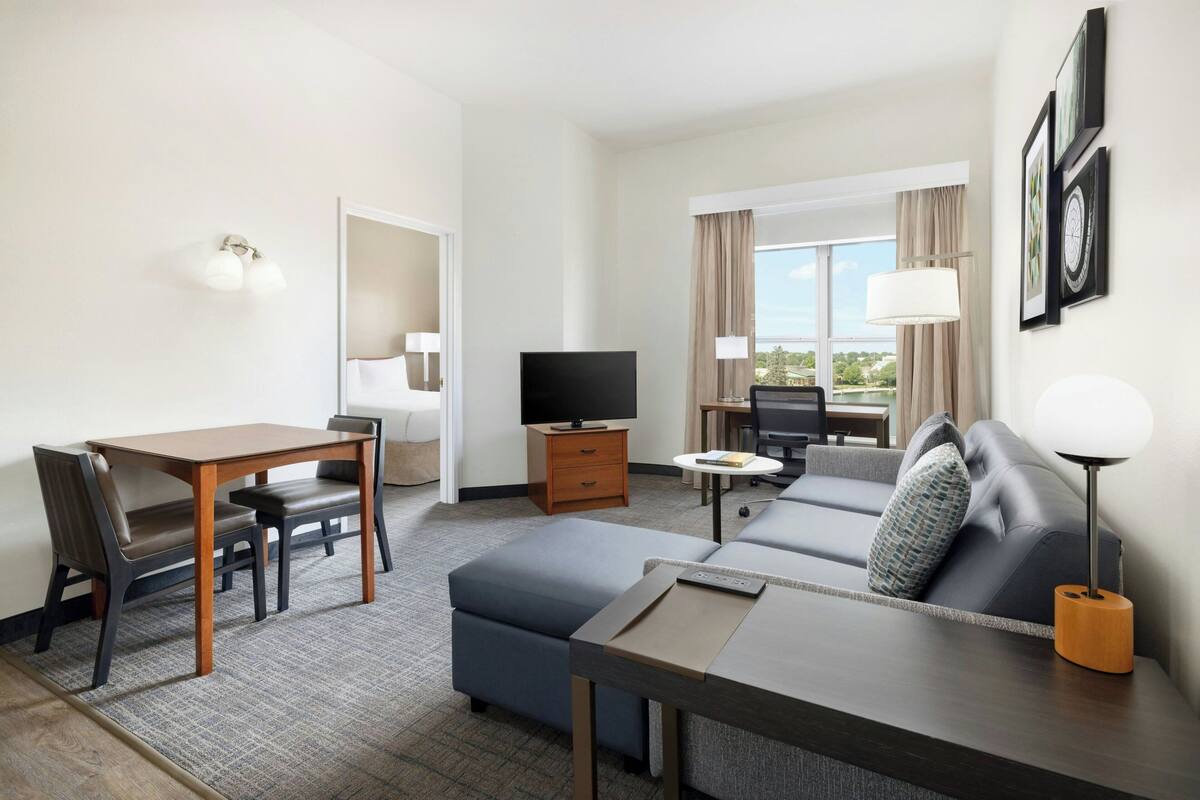 A hotel room with a dining area, a sofa, a TV, and a window with curtains.