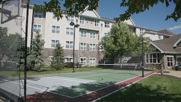 A tennis court with a net, surrounded by a building with multiple windows and a brick facade.