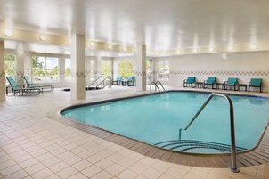Una piscina interior con suelo de baldosas, sillas de descanso y grandes ventanales.