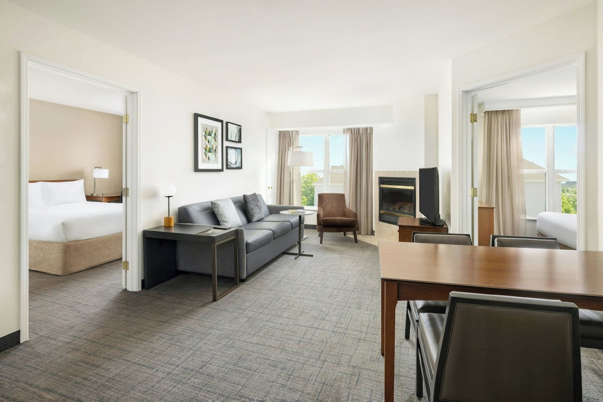 A hotel room with a bed, a sofa, a TV, and a dining area.