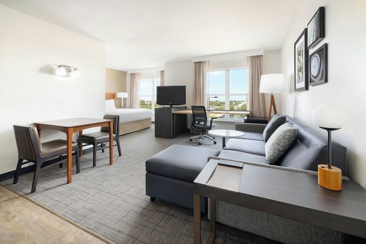 A hotel room with a bed, a desk with a chair, a sofa, a TV, and a lamp.