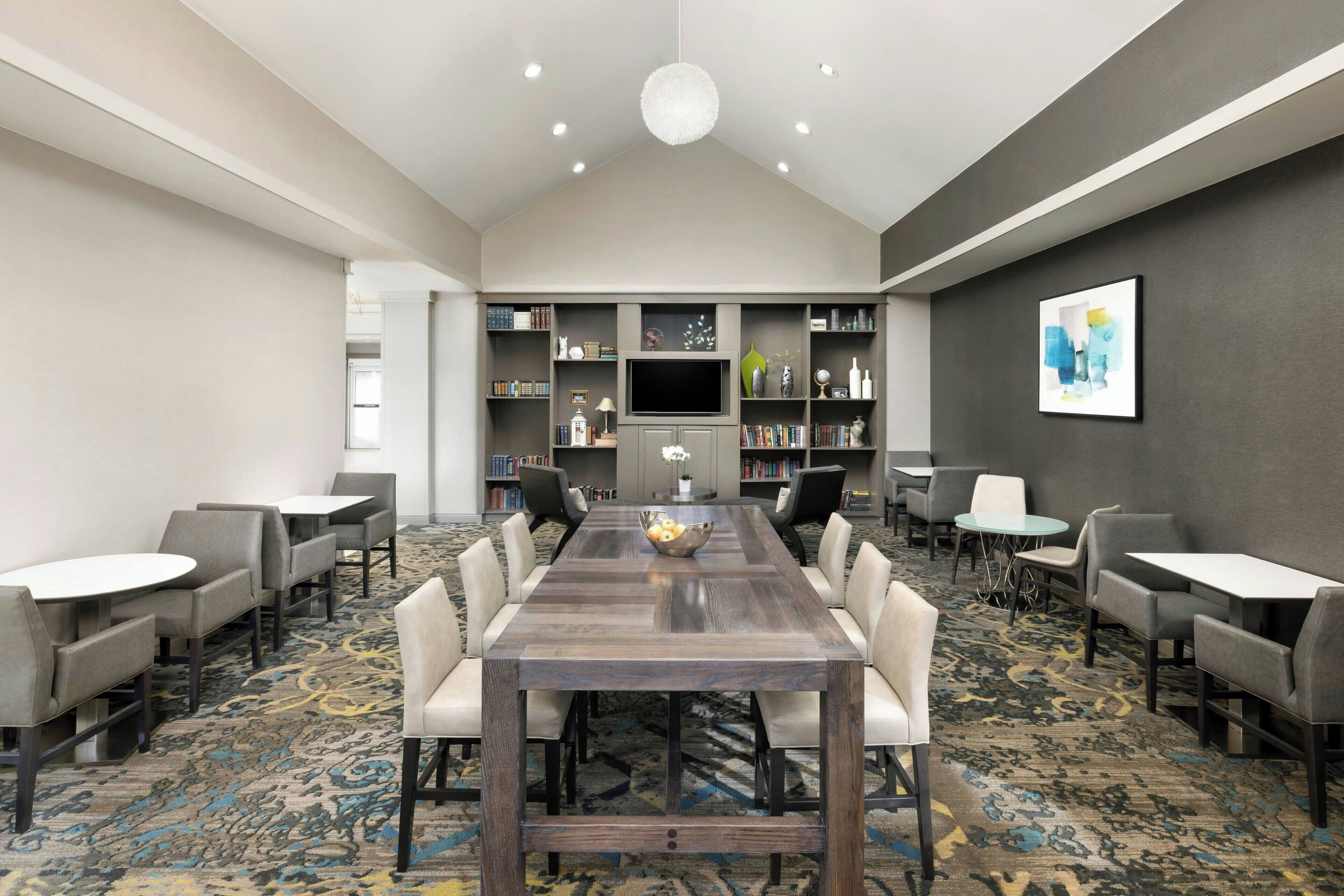 A conference room with a long table, chairs, a TV, bookshelves, and a patterned carpet.