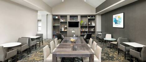 A conference room with a long table, chairs, a TV, bookshelves, and a patterned carpet.
