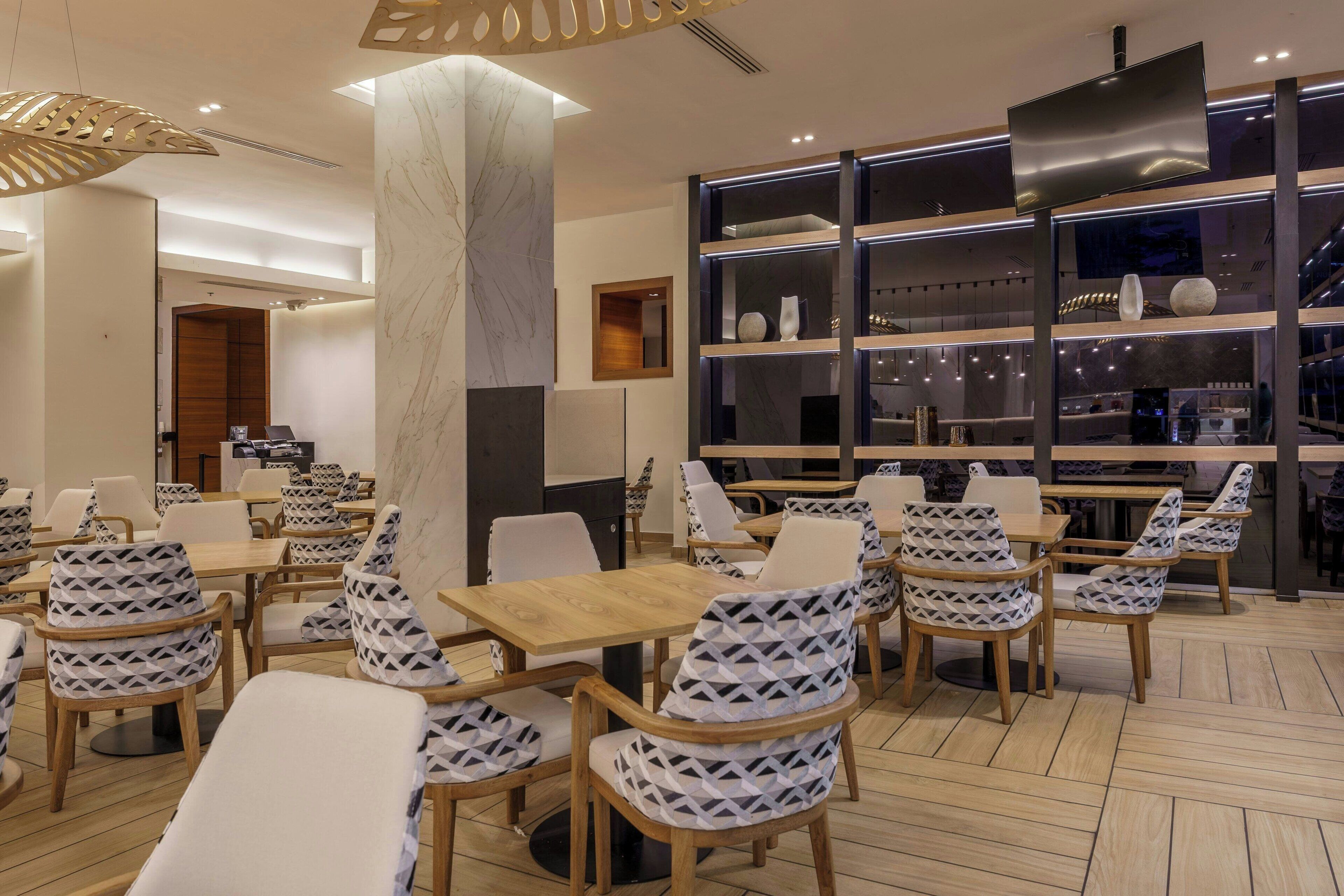 En modern restaurang med träbord och stolar med mönster, en marmorkolonn och en utställning av dekorativa föremål.