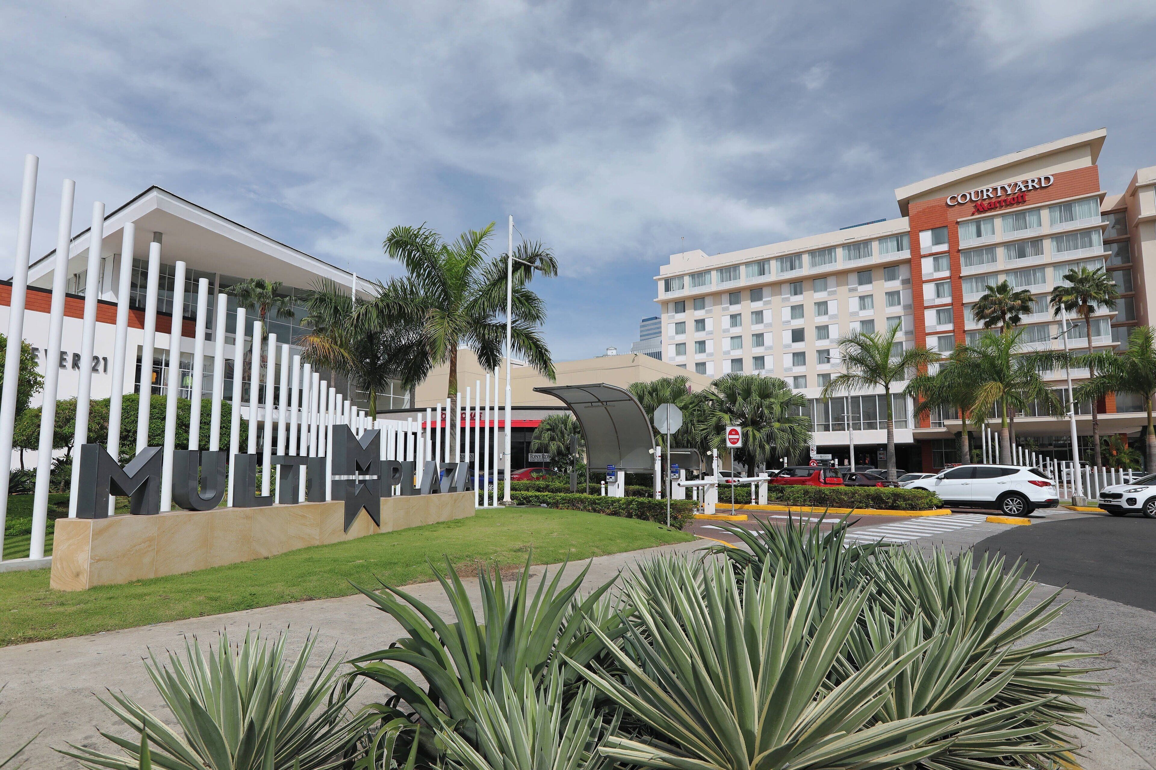 Un hotel de diseño moderno, con un llamativo letrero 'Courtyard', un césped bien cuidado y un estacionamiento con varios automóviles.