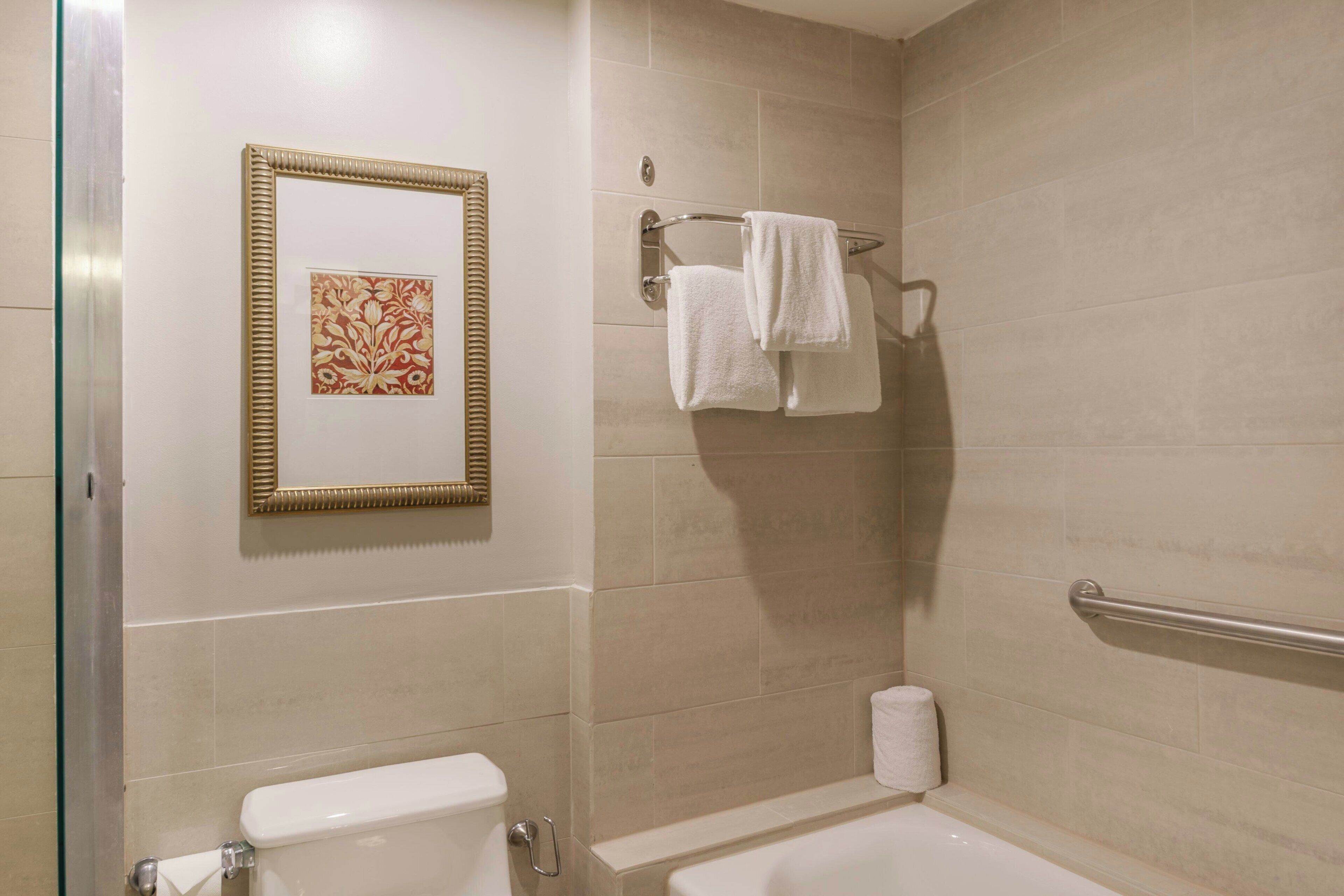 A bathroom with a toilet, a bathtub, a towel rack with towels, and a framed artwork on the wall.