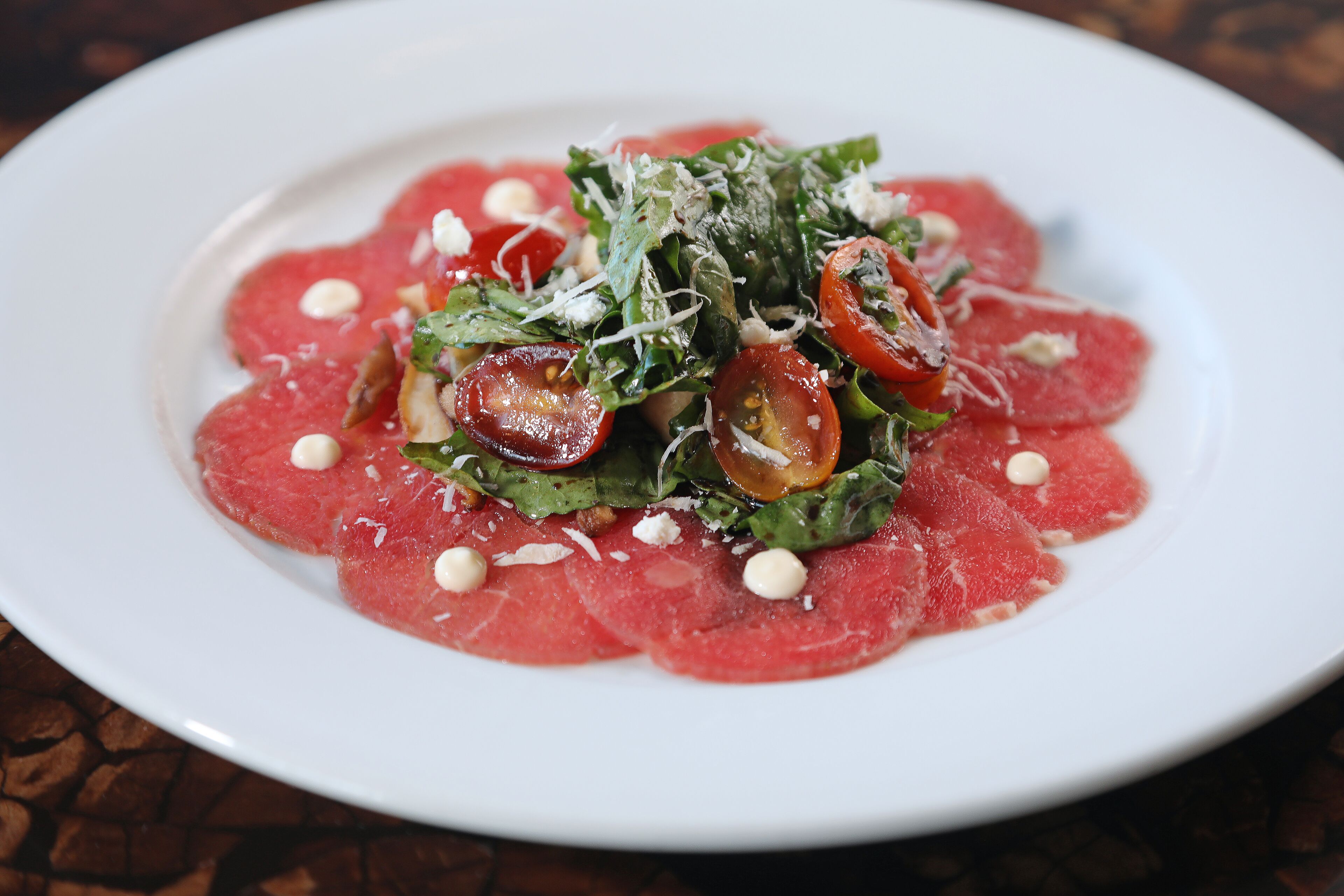 A plate of food with thinly sliced red meat, green leaves, and cherry tomatoes.