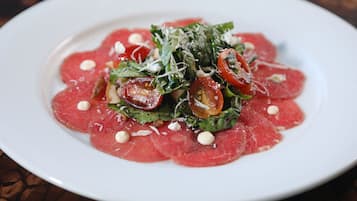 A plate of food with thinly sliced red meat, green leaves, and cherry tomatoes.