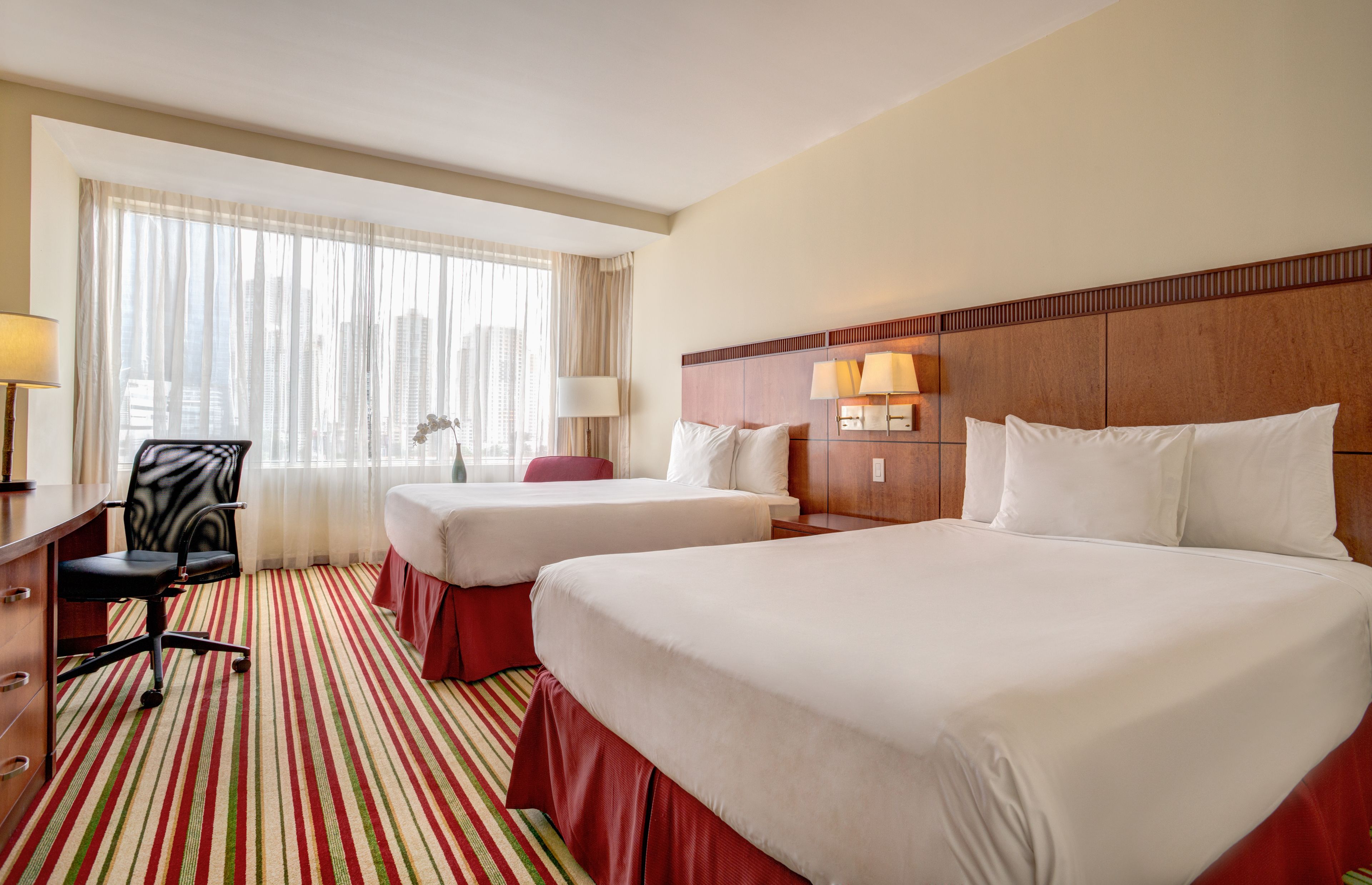 Een hotelkamer met twee bedden, een bureau, een stoel en een raam met gordijnen.