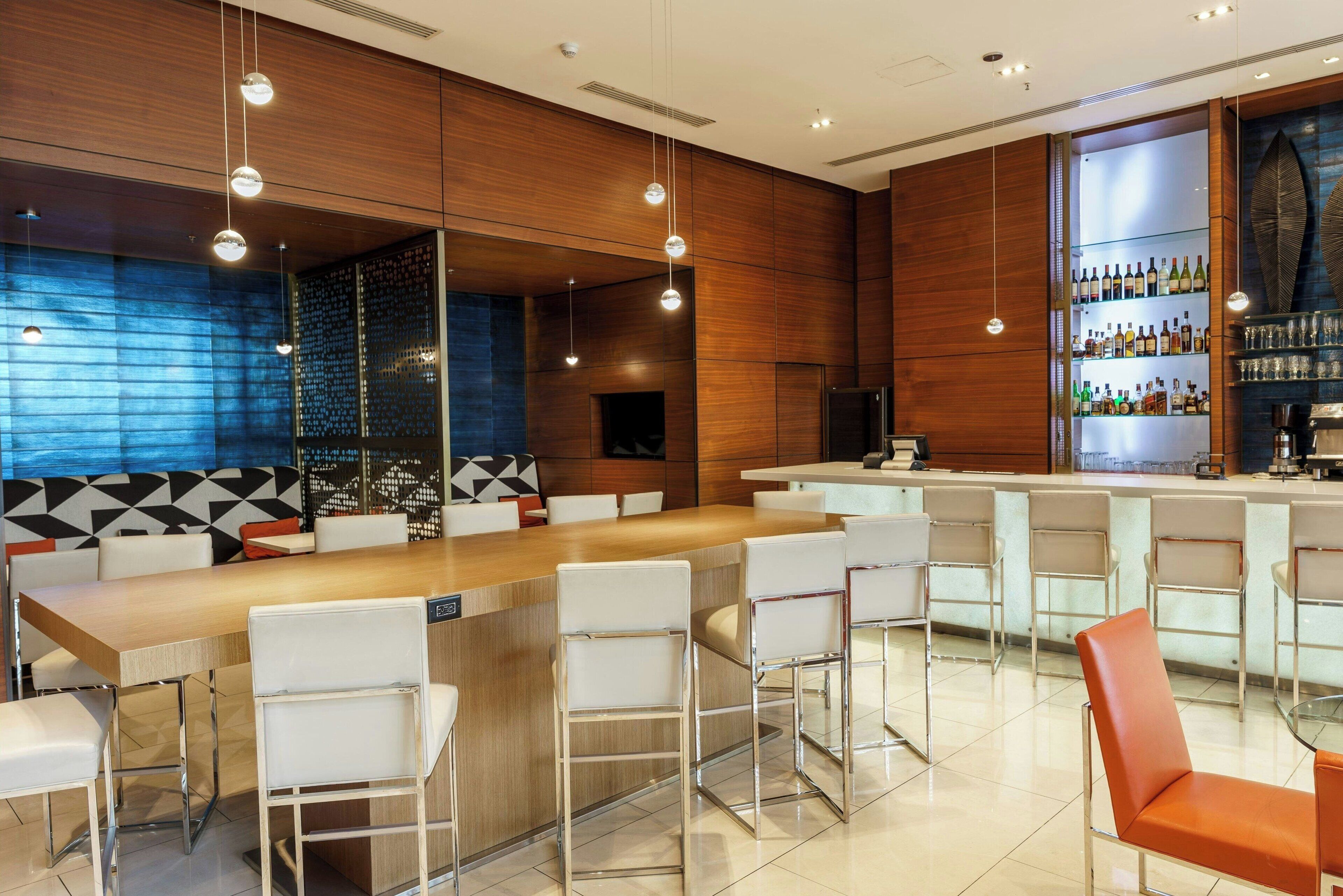 A modern bar area with a long counter, white bar stools, and a wooden accent wall.