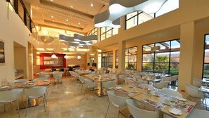 A spacious dining area with multiple tables and chairs, large windows offering views of the outdoors, and a modern ceiling design with hanging lights. - Fiesta Inn Nogales (Nogales)