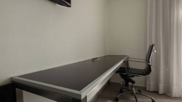 Un escritorio largo y estrecho con una silla, un televisor montado en la pared y una ventana con cortinas.