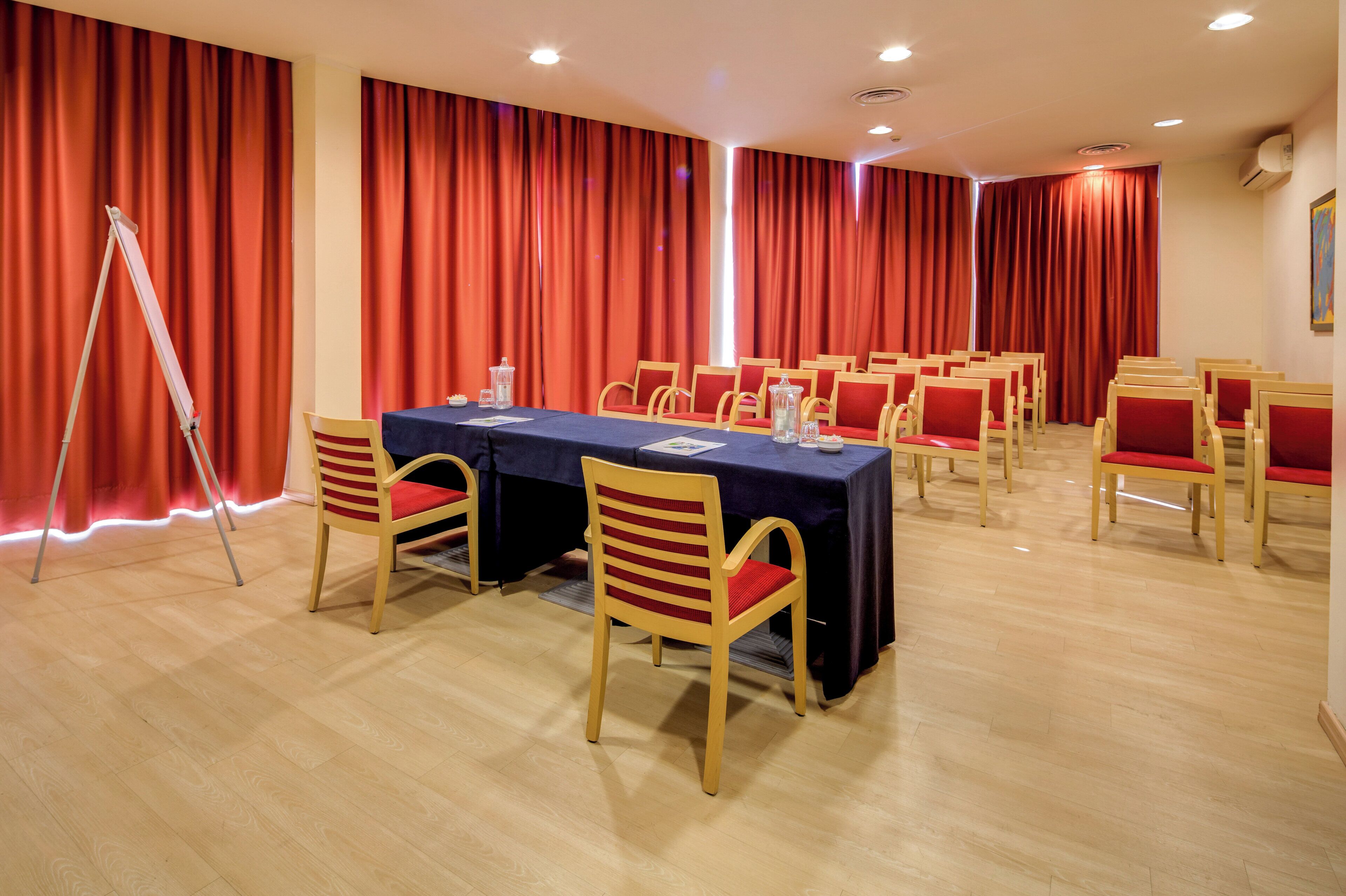 Una sala de conferències amb una taula llarga, cadires i cortines vermelles.