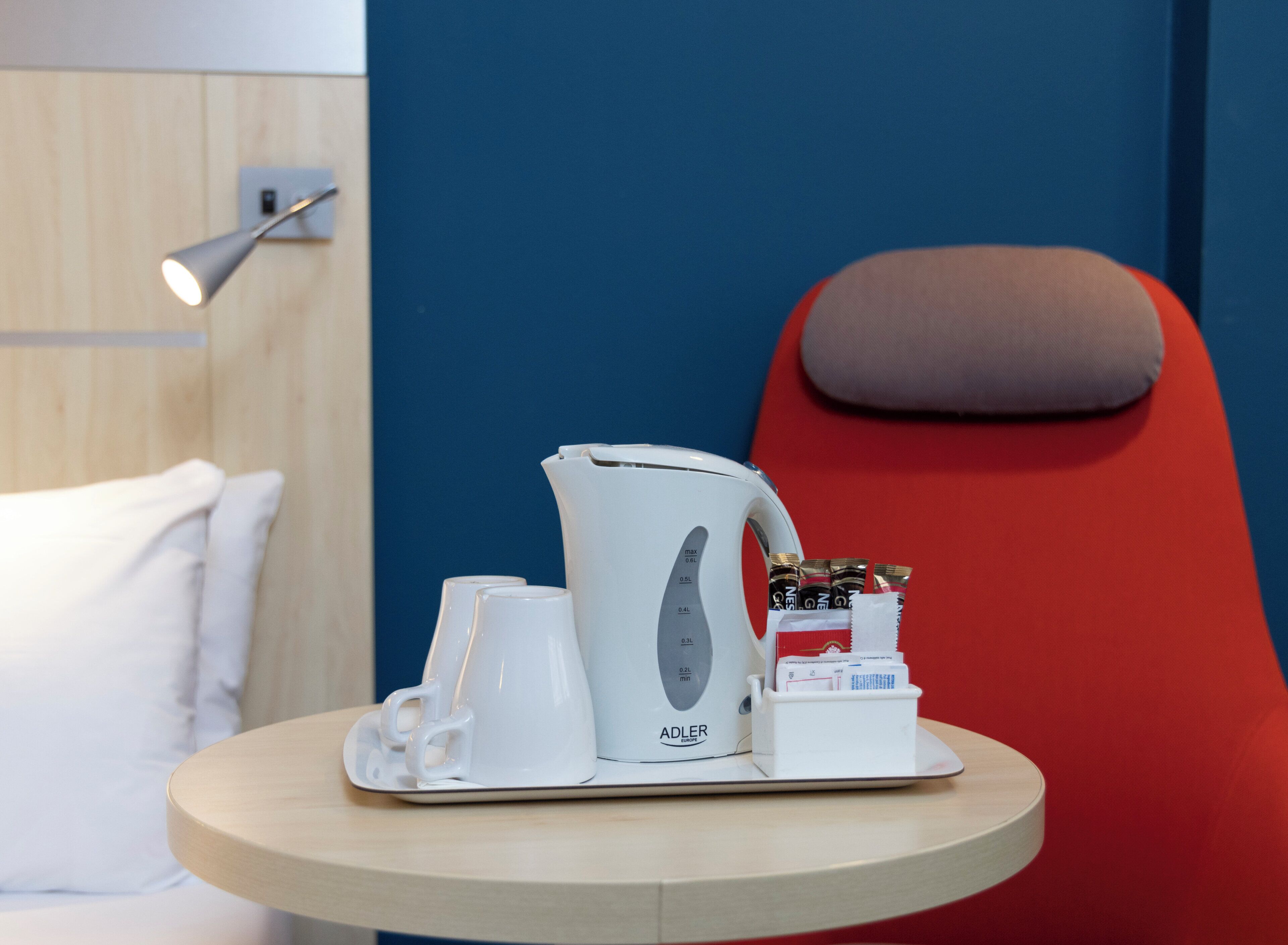 Ein Hotelzimmer mit einem Bett, einem runden Tisch, einer Kaffeemaschine, Tassen und einer kleinen Taschentuchbox.