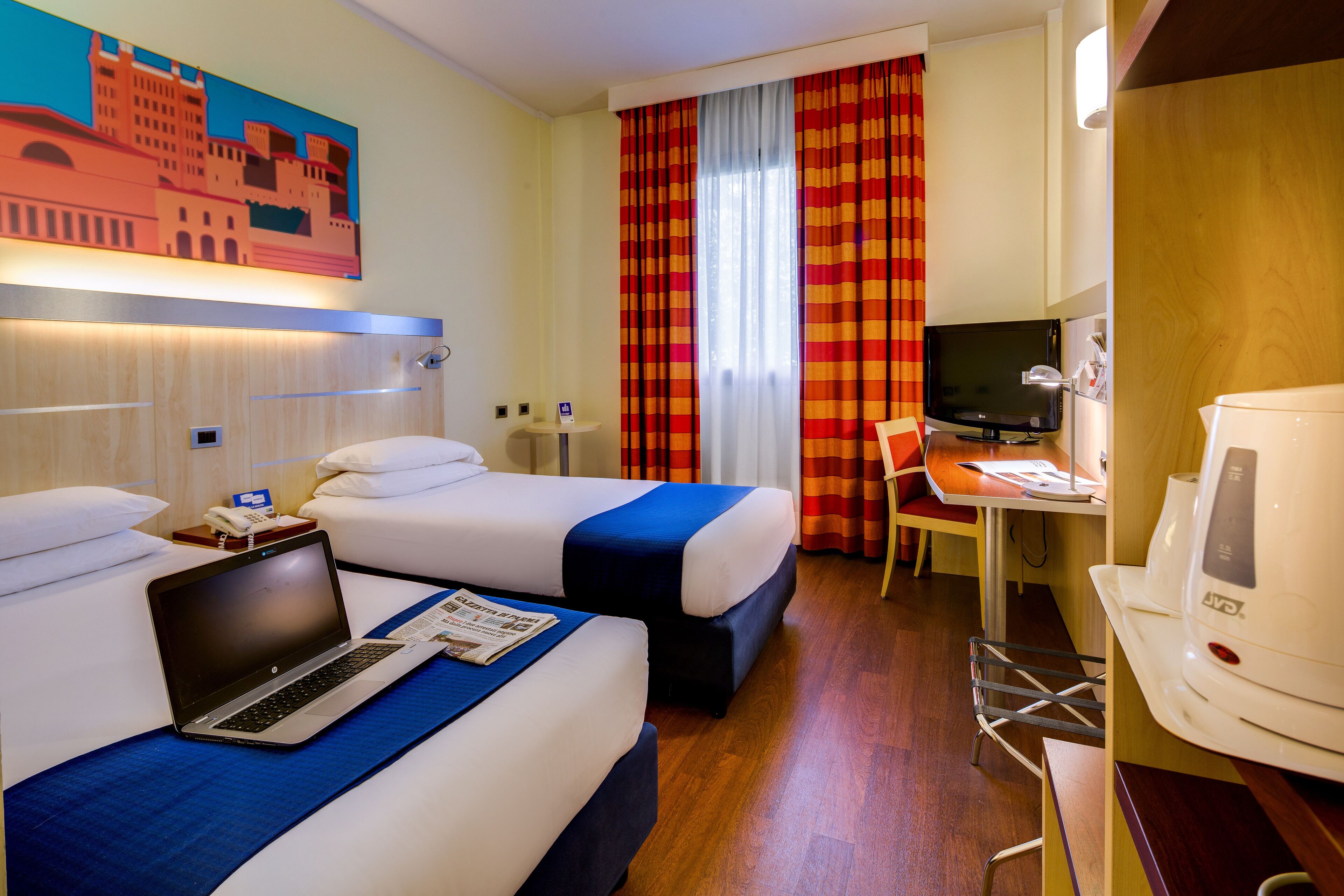 Habitación de hotel con dos camas, un escritorio con una computadora portátil, televisor y cafetera.