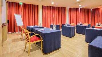 Ein Konferenzraum mit Tischen, Stühlen, einer Whiteboard-Tafel und roten Vorhängen.