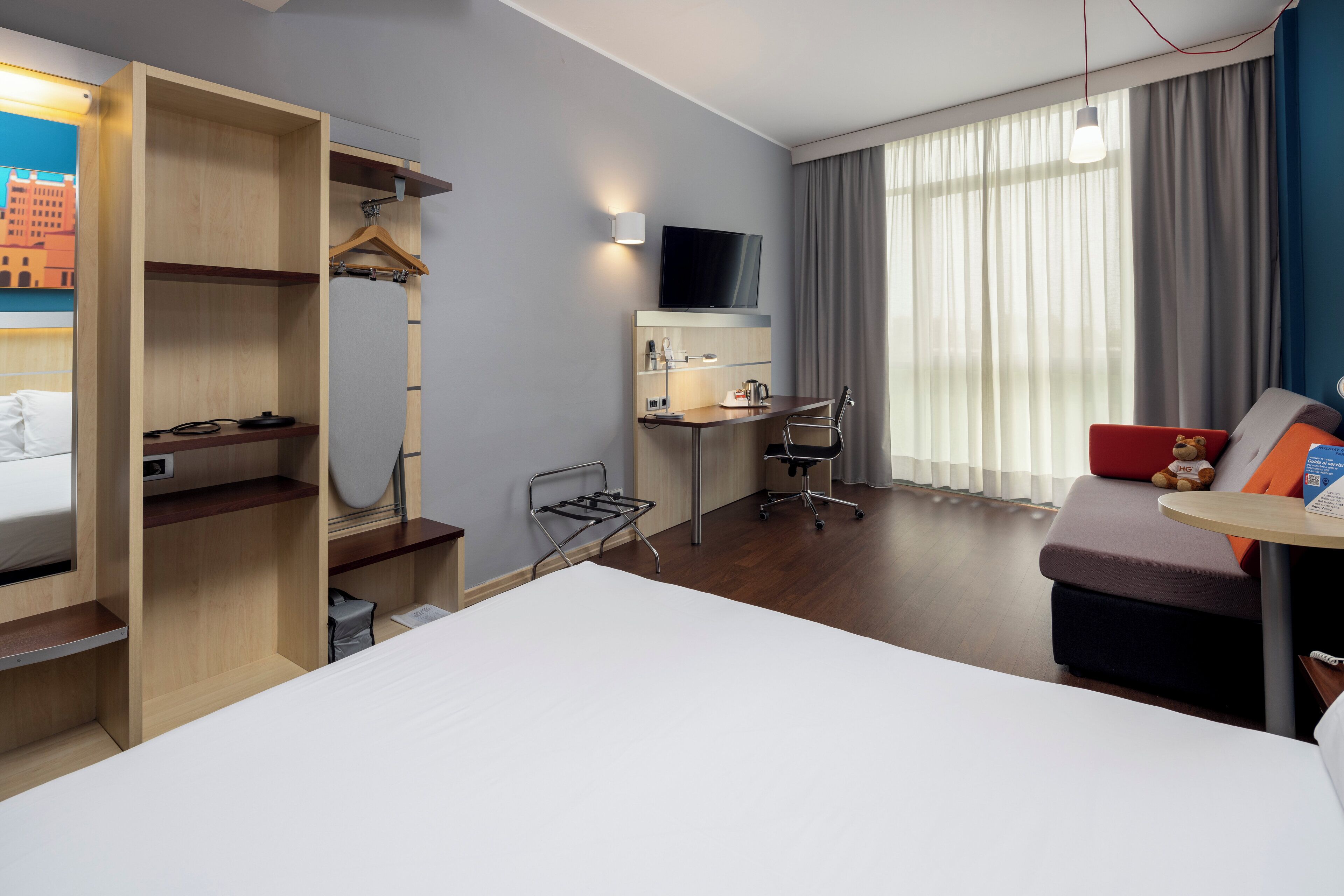 A hotel room with a bed, a desk with a chair, a TV, and a sofa with a table.