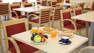A dining area with tables and chairs, a breakfast spread including fruits, pastries, and beverages.