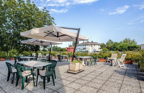 An outdoor patio area with tables and chairs, umbrellas, and potted plants.